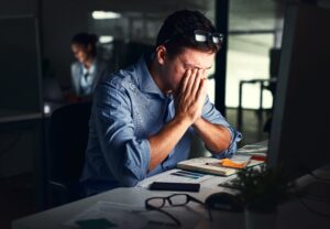 Stressed man working late in a dimly lit office, overwhelmed by deadlines and workplace pressure, highlighting the need for psychotherapy for stress management